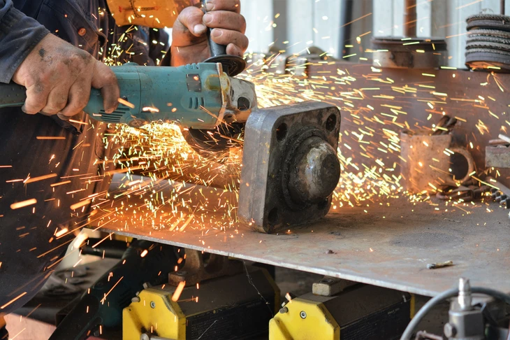 Atelier intérieur, artisan utilisant une meuleuse d'angle sur pièce métallique, étincelles oranges vives, mains expertes en action, travail de précision