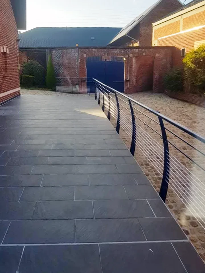 Terrasse extérieure contemporaine avec deux fauteuils en résine tressée noire sur dallage pierre naturelle
