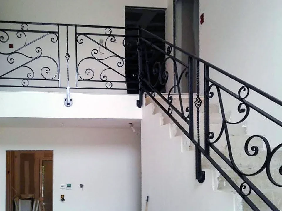 Espace de vie moderne avec escalier métallique noir, mur en briques blanches peintes, bureau sous escalier avec chaise ergonomique, canapé gris, table basse design