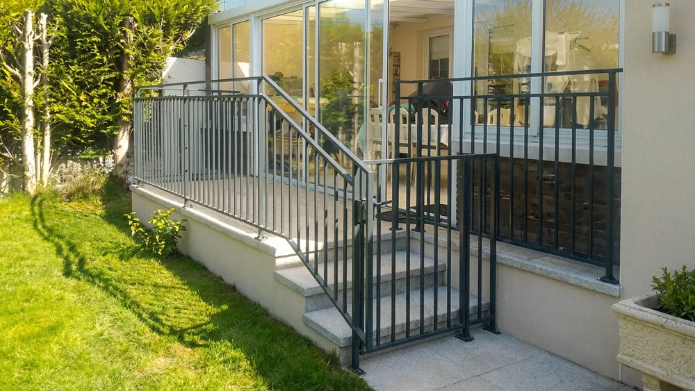 Espace de vie moderne avec escalier métallique noir, mur en briques blanches peintes, bureau sous escalier avec chaise ergonomique, canapé gris, table basse design