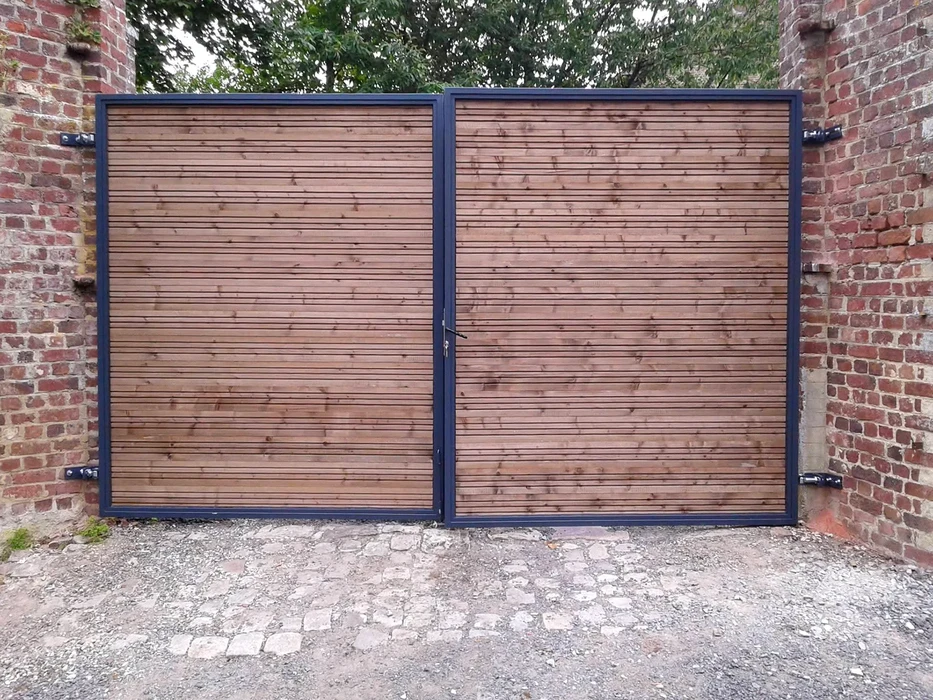 Entrée résidentielle avec portail automatique en fer forgé orné de volutes décoratives, flanqué de piliers en béton blanc équipés d'interphones et luminaires