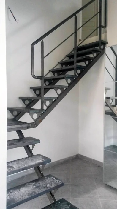 Intérieur moderne avec escalier suspendu à marches en bois et structure métallique noire, rampe forgée décorative