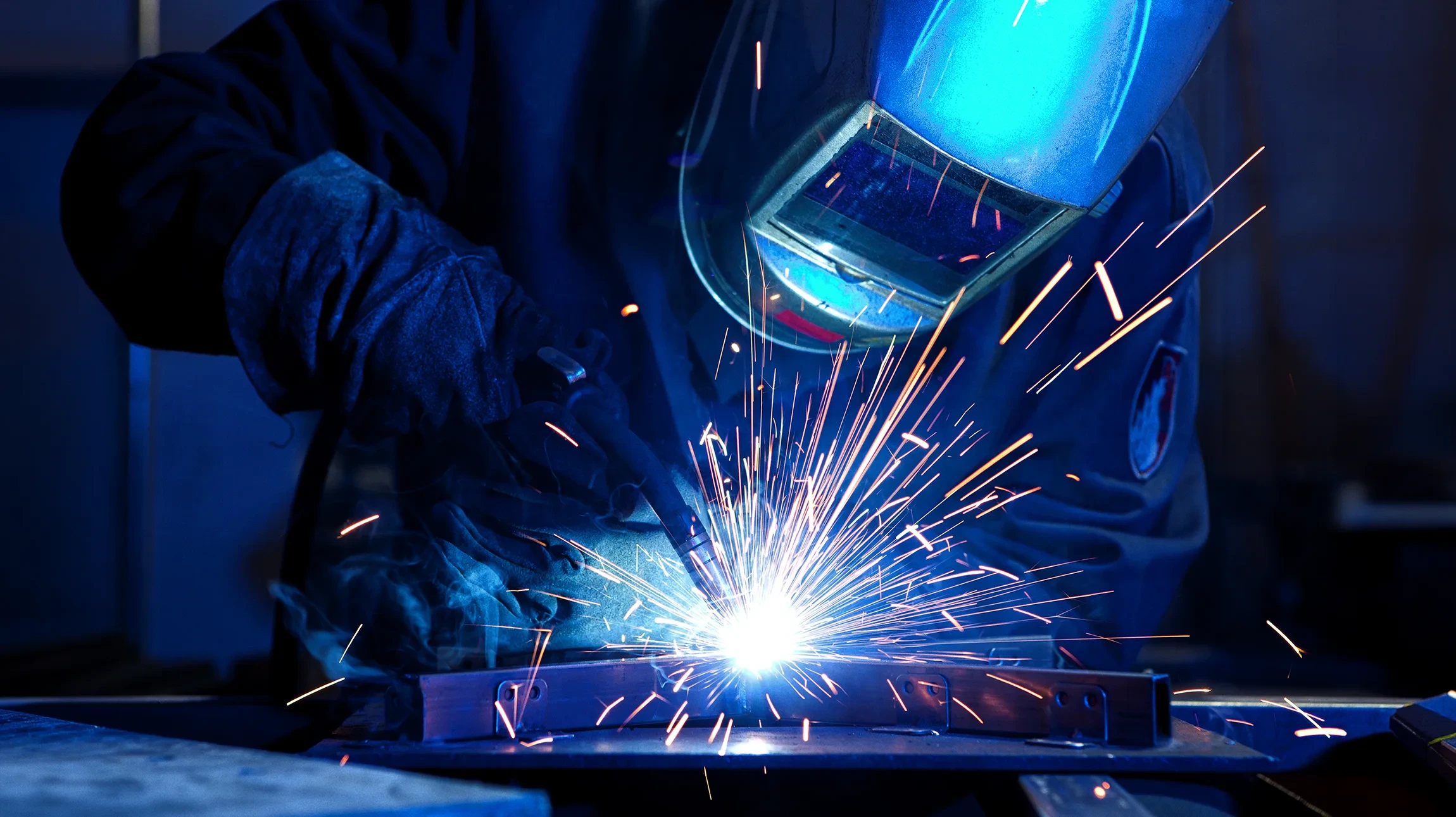 Soudeur professionnel en combinaison de travail et masque de protection exécutant une soudure à l'arc sur une structure métallique avec rampe et barreaux