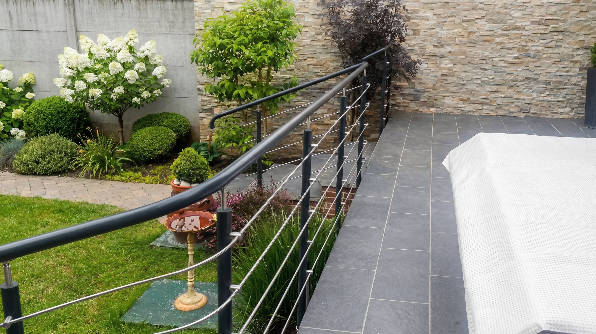 Balcon d'appartement avec deux fauteuils en résine tressée et coussins beiges, planchers en composite, garde-corps métallique noir