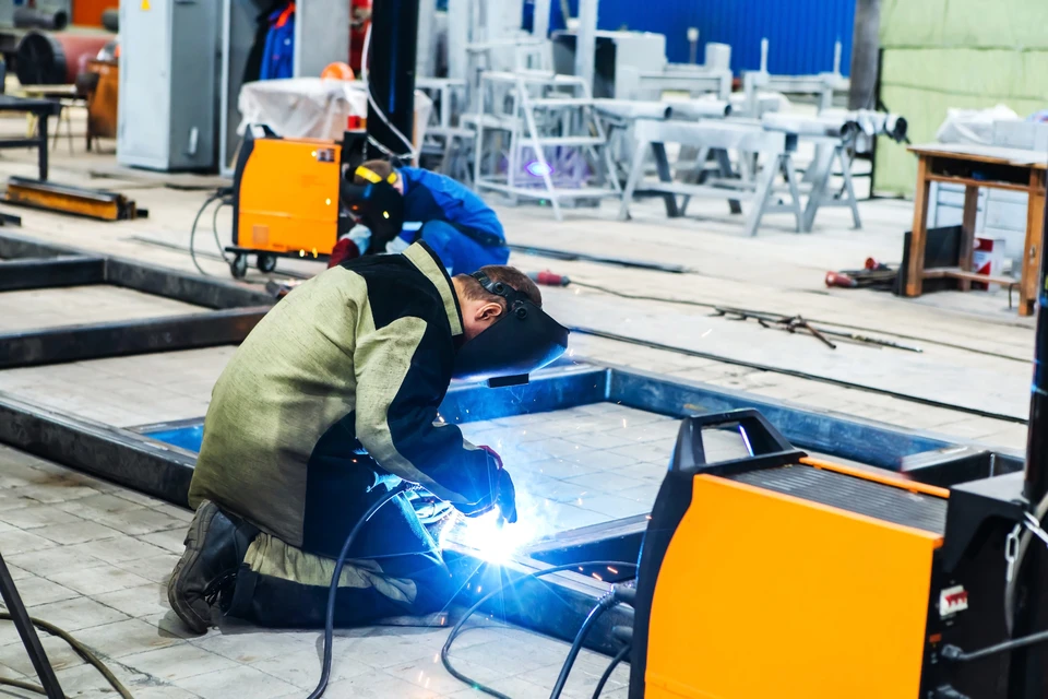 Soudeur professionnel en action dans un atelier sombre, portant masque de protection et vêtements de sécurité, réalisant une soudure sur métal avec projection d'étincelles lumineuses